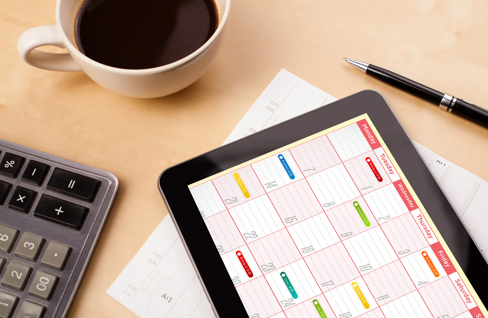 Workplace with tablet pc showing calendar and a cup of coffee on a wooden work table close-up Workplace with tablet pc showing calendar and a cup of coffee on a wooden work table close-up